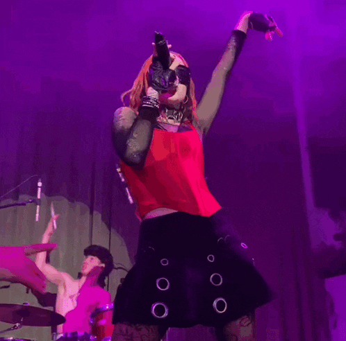 a woman in a red top and black skirt is singing into a microphone on stage