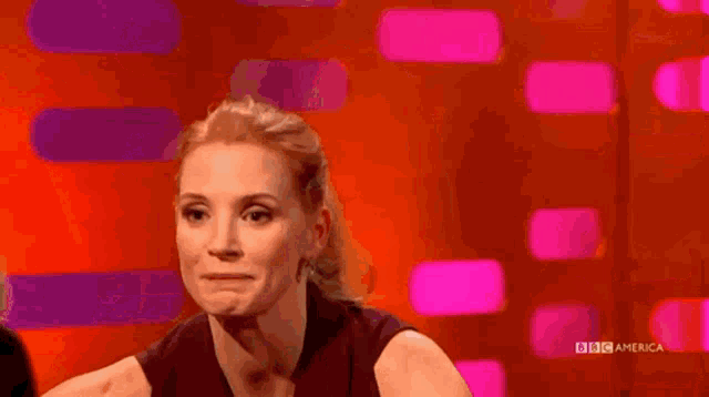 a woman is smiling while sitting in front of a screen that says bbc america