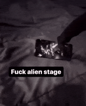 a person holding a cell phone on a bed with the words " fuck alien stage " above it