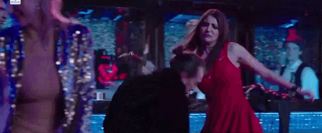 a man and a woman are dancing on a stage in a dark room . the woman is wearing a red dress .