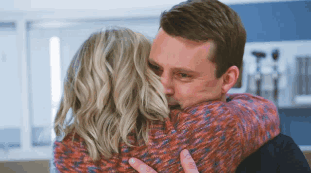 a man in a red sweater is hugging a blonde woman