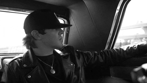 a man wearing a black hat and a leather jacket is sitting in a car