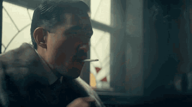 a man in a fur coat is smoking a cigarette in front of a window