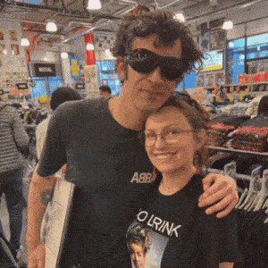 a man wearing sunglasses stands next to a woman wearing a black t-shirt that says olrink