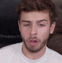 a close up of a man with a beard wearing a white t-shirt making a funny face .