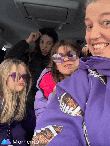 a woman wearing a purple jacket with a football on the sleeve takes a selfie with her three daughters