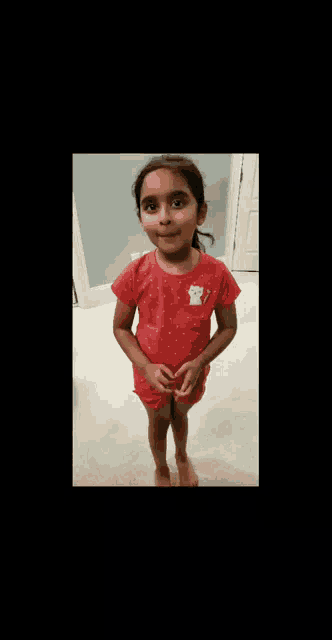 a little girl wearing a red shirt with a teddy bear on it is smiling