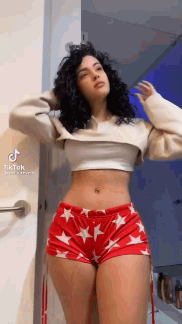 a woman with curly hair is wearing a white crop top and red shorts with white stars .