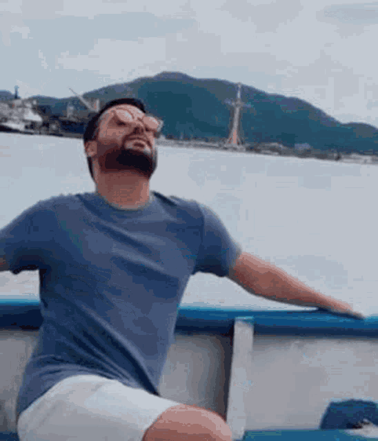 a man with a beard and sunglasses is sitting on a boat with his arms outstretched .