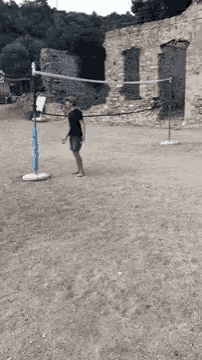 a man is standing next to a volleyball net in a dirt field .