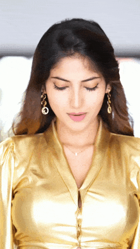 a close up of a woman wearing a gold shirt and earrings