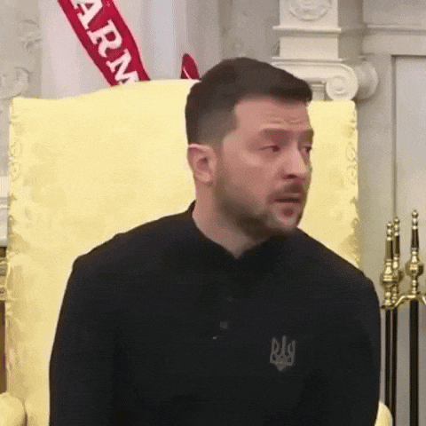 a man in a black shirt is sitting in a chair with a flag in the background .
