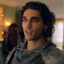 a young man with curly hair is wearing a knight 's armor and chain mail .
