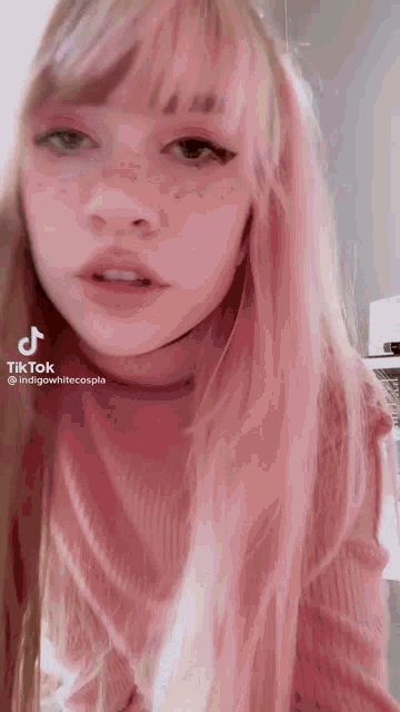 a girl with pink hair and freckles is wearing a pink sweater and a choker .