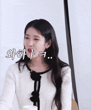 a woman wearing a white sweater and black trim is laughing with her mouth wide open