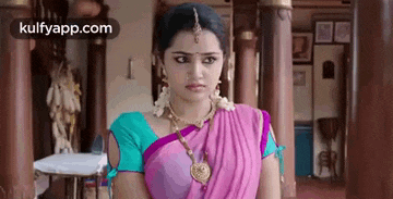 a woman in a pink and blue saree is standing in a hallway .