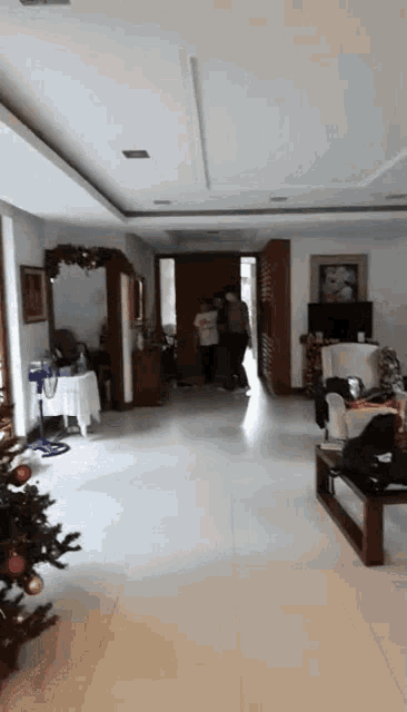 a group of people are standing in a living room with a christmas tree in the middle