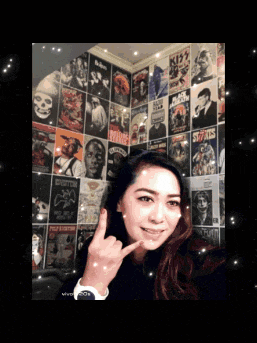 a woman giving a peace sign in front of a wall of posters including one for kiss