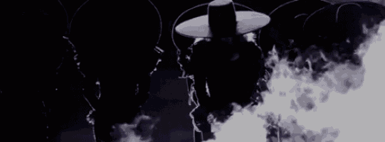 a man in a sombrero is standing in front of a fire in the dark .