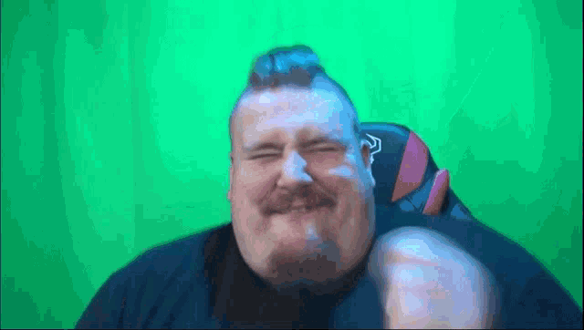 a fat man with a beard is sitting in front of a green screen .