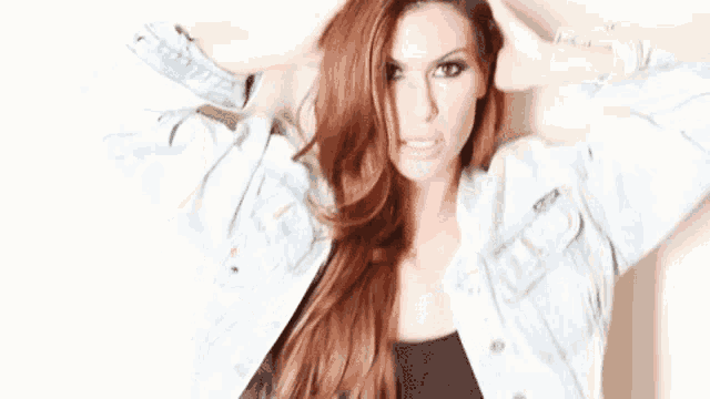 a woman wearing a denim jacket and a black top is standing in front of a white wall .