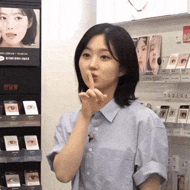 a woman making a shhh sign in front of a display of eye shadows