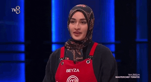 a woman wearing a hijab and an apron is sitting on a stage .