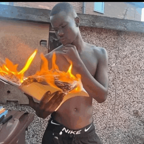 a shirtless man in nike shorts is holding a burning book