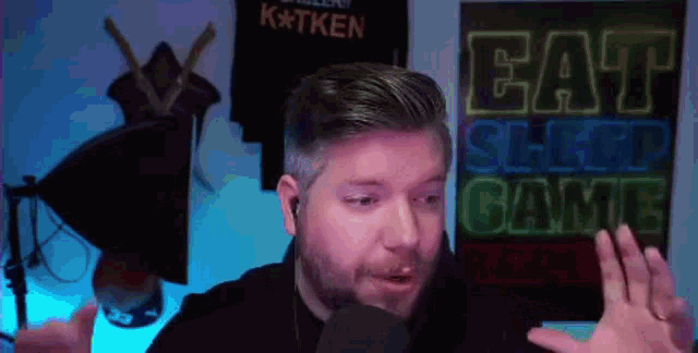 a man is talking into a microphone in front of a sign that says " eat sleep game "