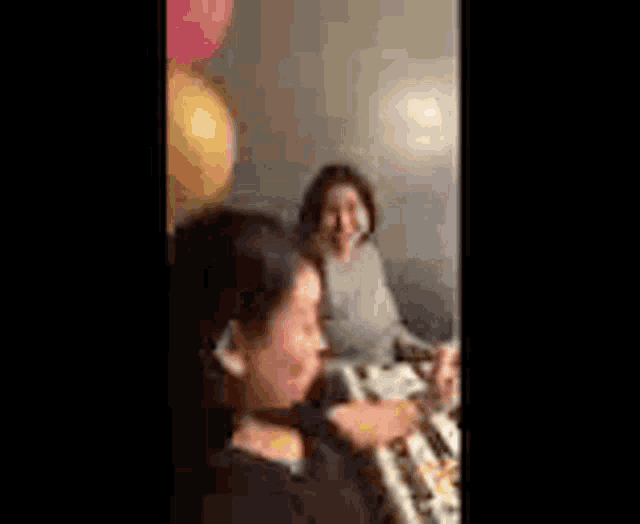 two women are sitting at a table with balloons and a woman is playing a keyboard .
