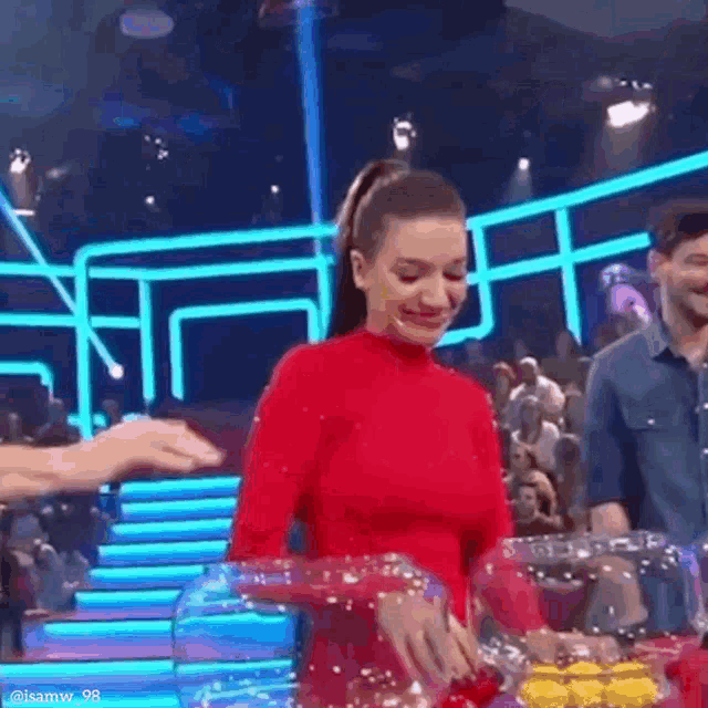 a woman in a red dress is standing in front of a glass container filled with yellow balls .