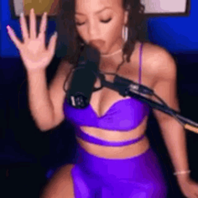 a woman in a purple crop top and shorts is sitting in front of a microphone .