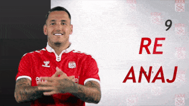 a man in a red hummel shirt stands in front of a sign that says anaj