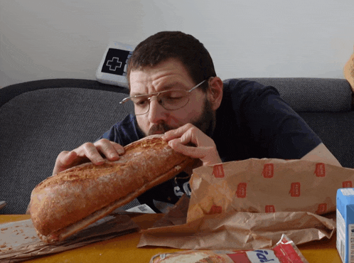 a man is eating a loaf of bread from a bag that says ' bakery ' on it