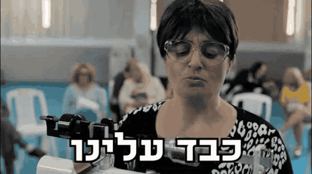 a woman wearing glasses and a leopard print shirt is holding a machine with hebrew writing above it