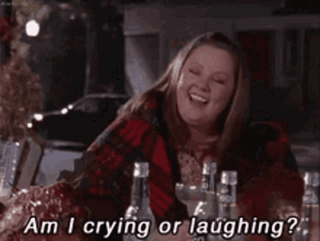 a woman is crying and laughing while sitting at a table with bottles of alcohol .