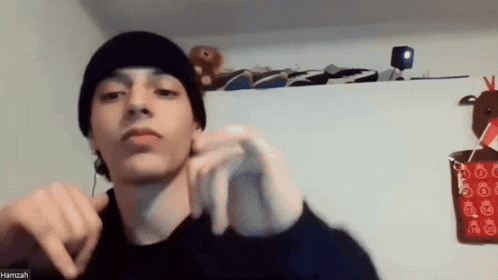 a young man wearing a black beanie and a black sweater is pointing at the camera .