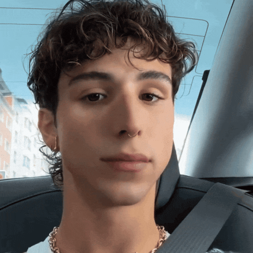 a young man with curly hair and a nose ring is wearing a seat belt