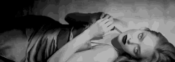 a black and white photo of a woman laying down holding a knife .