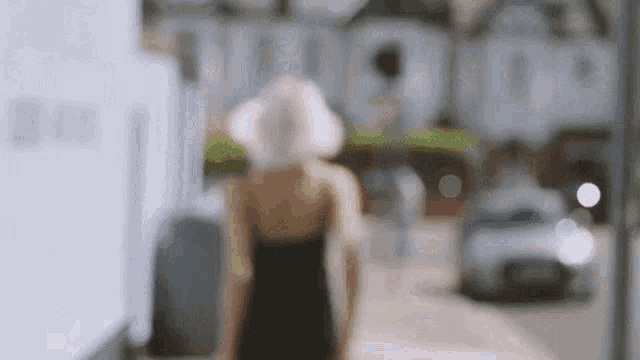 a woman in a black dress and white hat is walking down the street