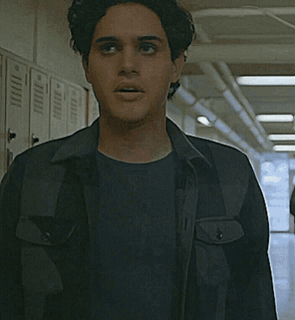 a man in a black jacket stands in a hallway with lockers