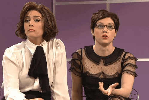 two women sitting next to each other with one wearing glasses and a white shirt