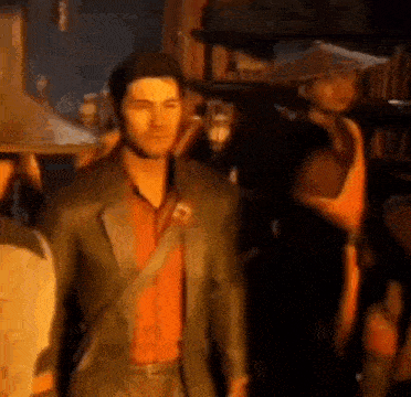 a man in a suit and red shirt is standing next to a group of people in a room .