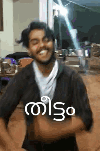 a man in a black jacket is smiling and dancing in front of a sign that says ' telugu ' in white letters