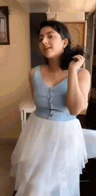 a woman in a blue top and a white skirt is standing in a room .