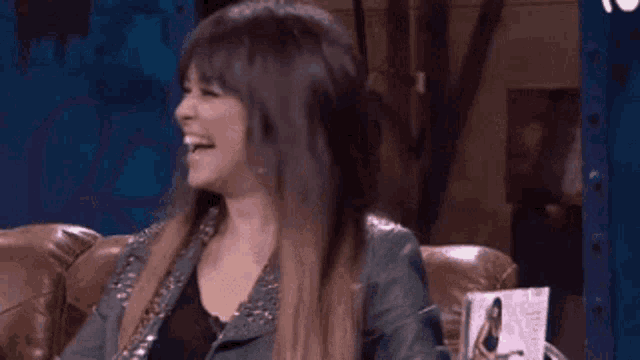 a woman in a leather jacket is sitting on a couch smiling .