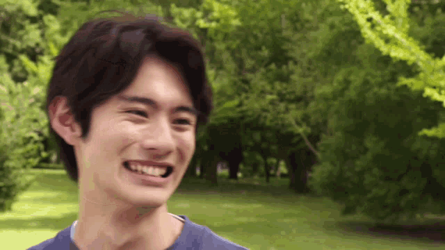 a man in a blue shirt is smiling in a park