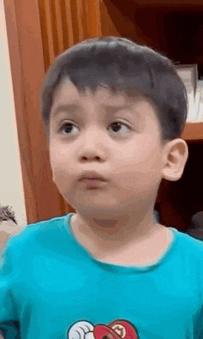 a young boy in a blue shirt is making a funny face and looking at the camera .