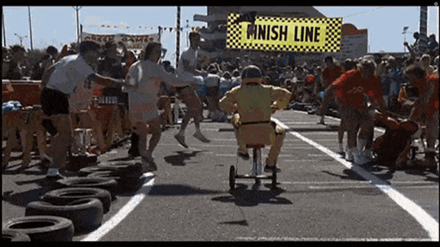 a man in a yellow suit is riding a go kart on a race track with a finish line sign in the background .