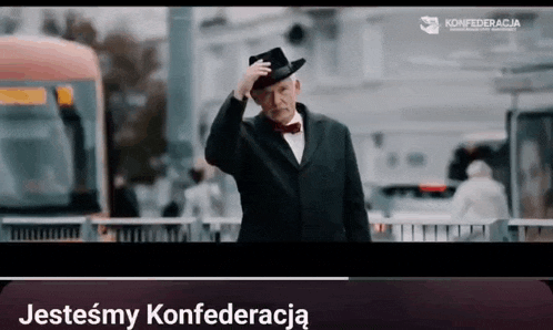 a man in a suit and bow tie is standing in front of a bus and a sign that says jestesmy konfederacja